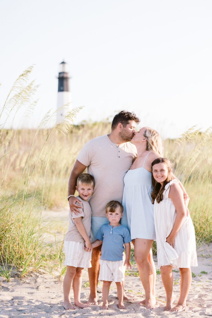 Parents kiss while embracing their children during a Tybee Island Family photo session.