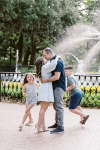 A candid moment with children running and playing while their parents kiss in front of Savannah's famous Forsyth Park fountain.