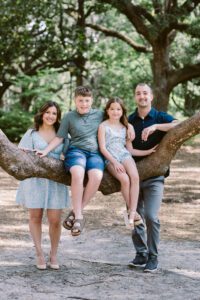 A family sits on a low live oak branch in Savannah's Forsyth Park for a portrait.